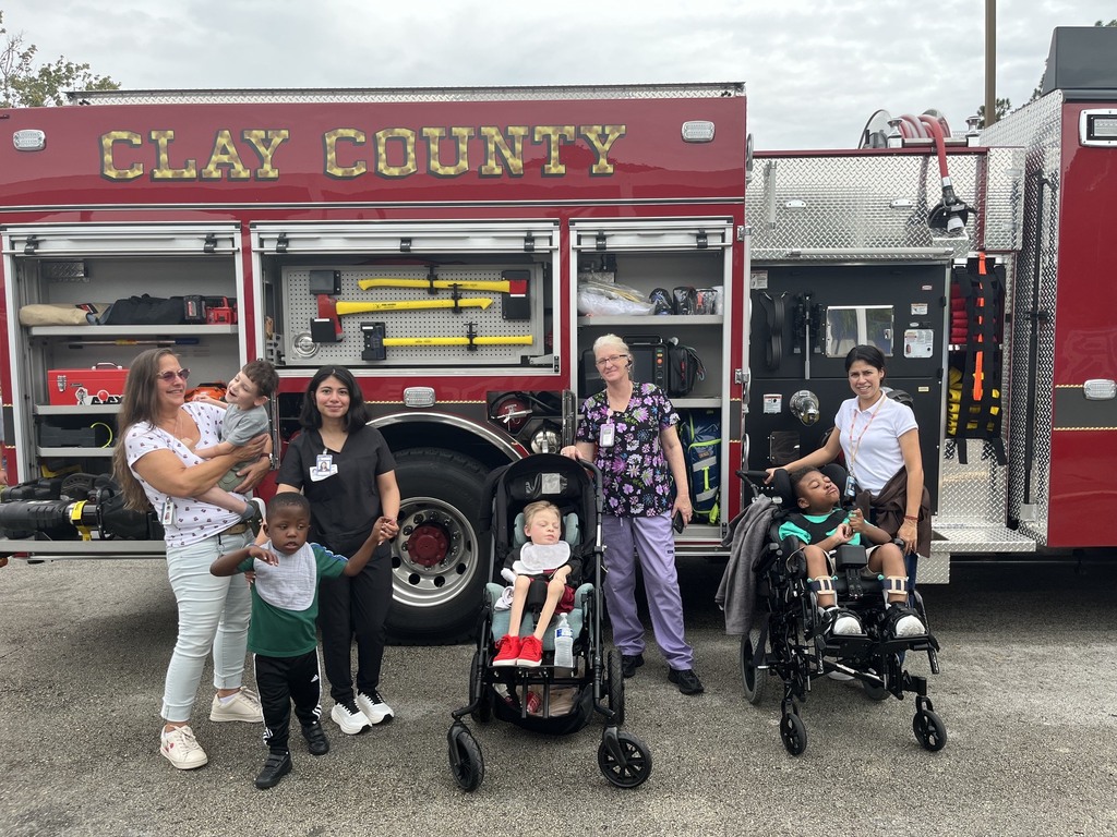 2 students in wheelchairs and two other students along with teachers stand in front of a fire truck.