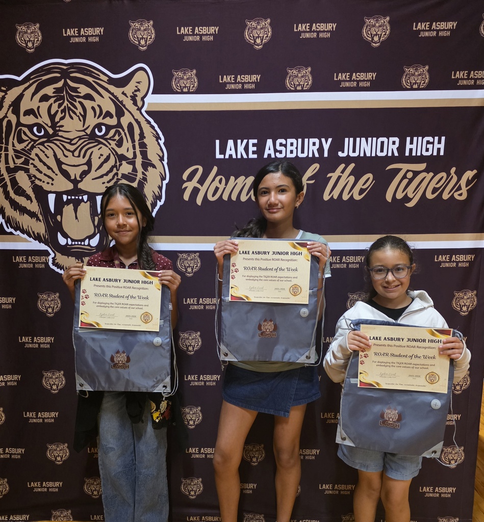 Three girls pose with certificates in front of a wall with a tiger logo and text.