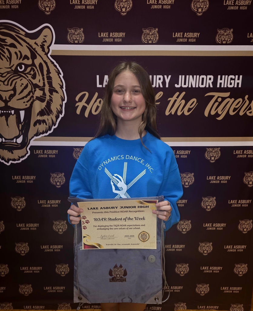 Girl holding a certificate in front of a wall with a tiger image and "Lake Asbury Junior High" text.