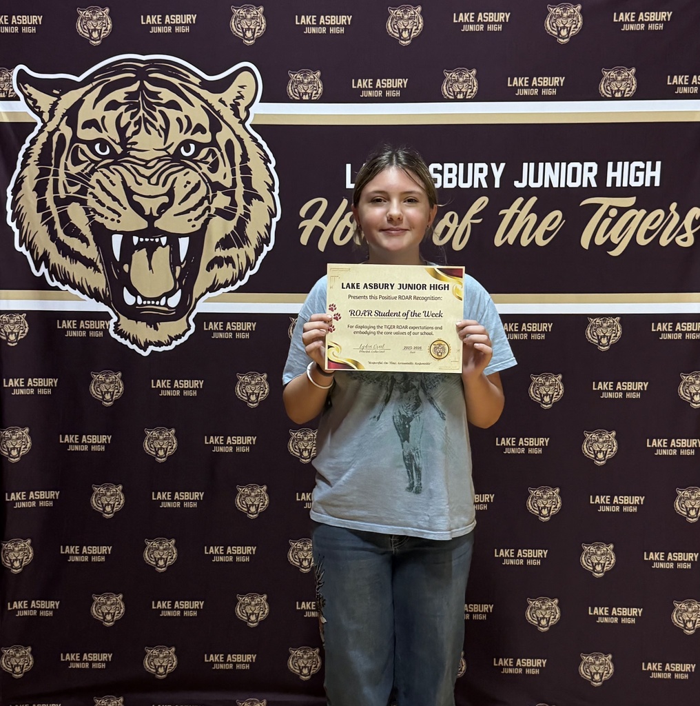 A young girl holds an award certificate in front of a tiger logo on a backdrop.