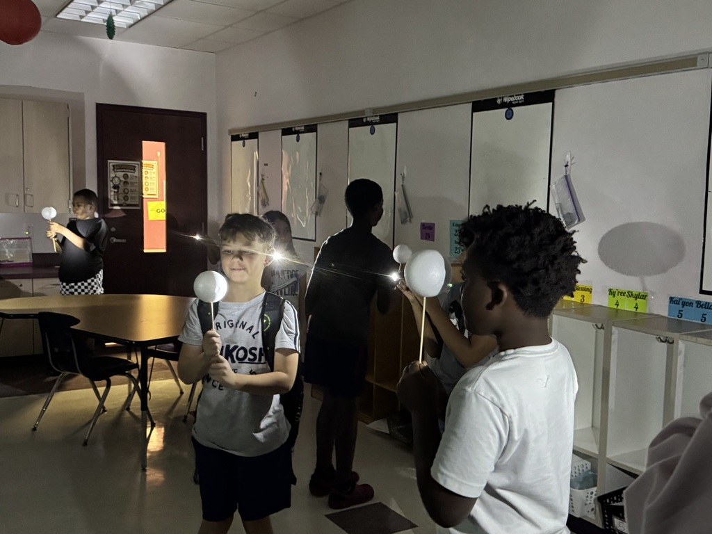 Students inside a classroom. One student holds a light-up object, and another student looks on.