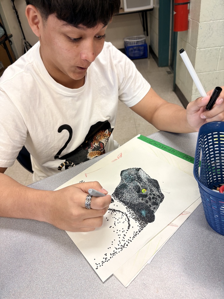 A student wearing a white t-shirt draws a picture of an animal on a paper.