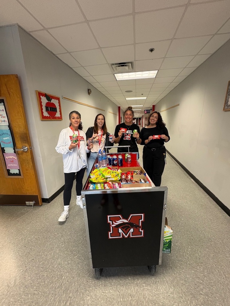 Four people in a hallway, smiling, with a cart full of items in front of them.