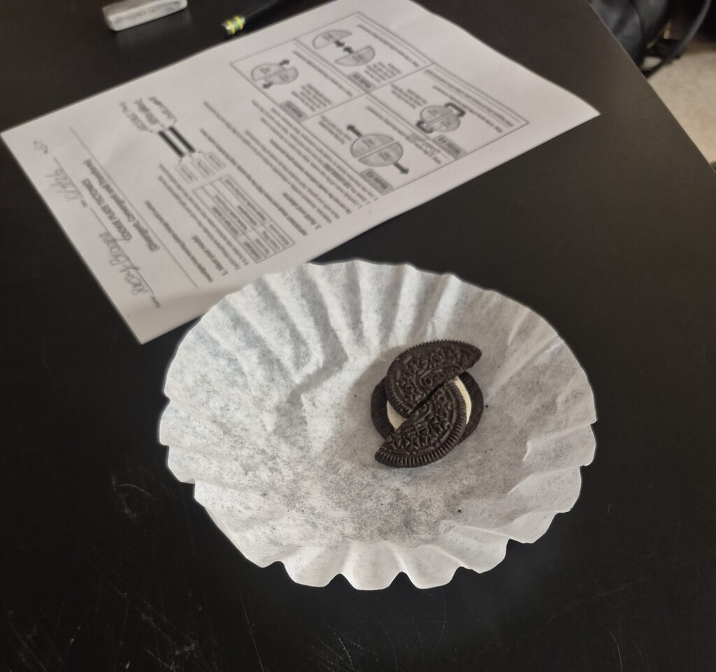 A plate with two cookies rests on a coffee filter, next to a folded paper with text on a dark surface.