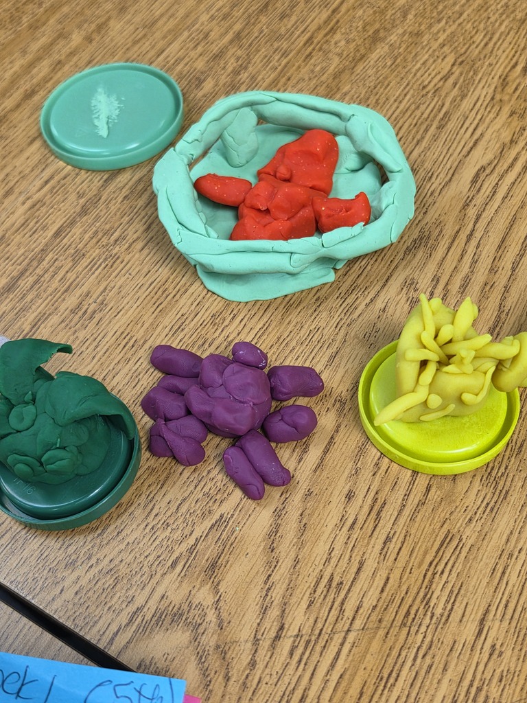Various colored playdough objects on a wooden table. These include a red figure, green, purple, and yellow shapes.