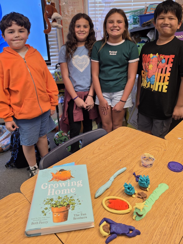 Four children stand around a table with a book titled "Growing Home" and various gardening tools on it.