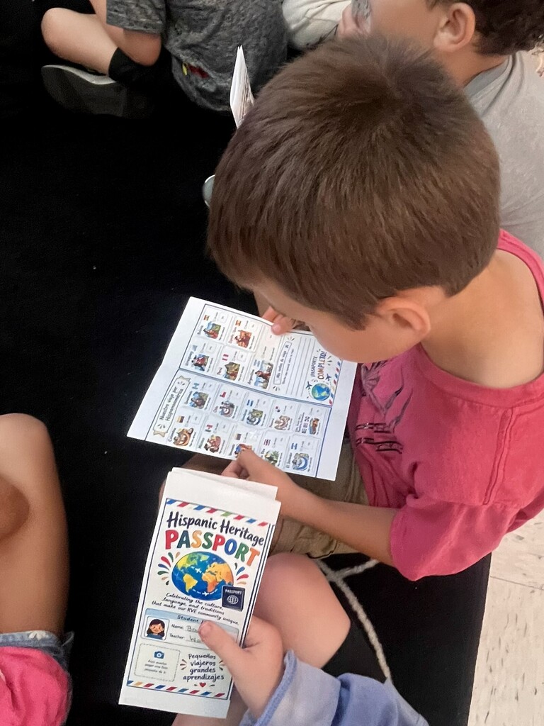 A young boy holds a book and studies it closely while seated with others on a floor.
