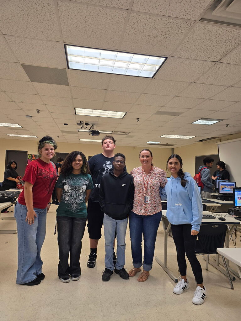 Five people in a classroom. They stand close to one another and appear to be smiling.