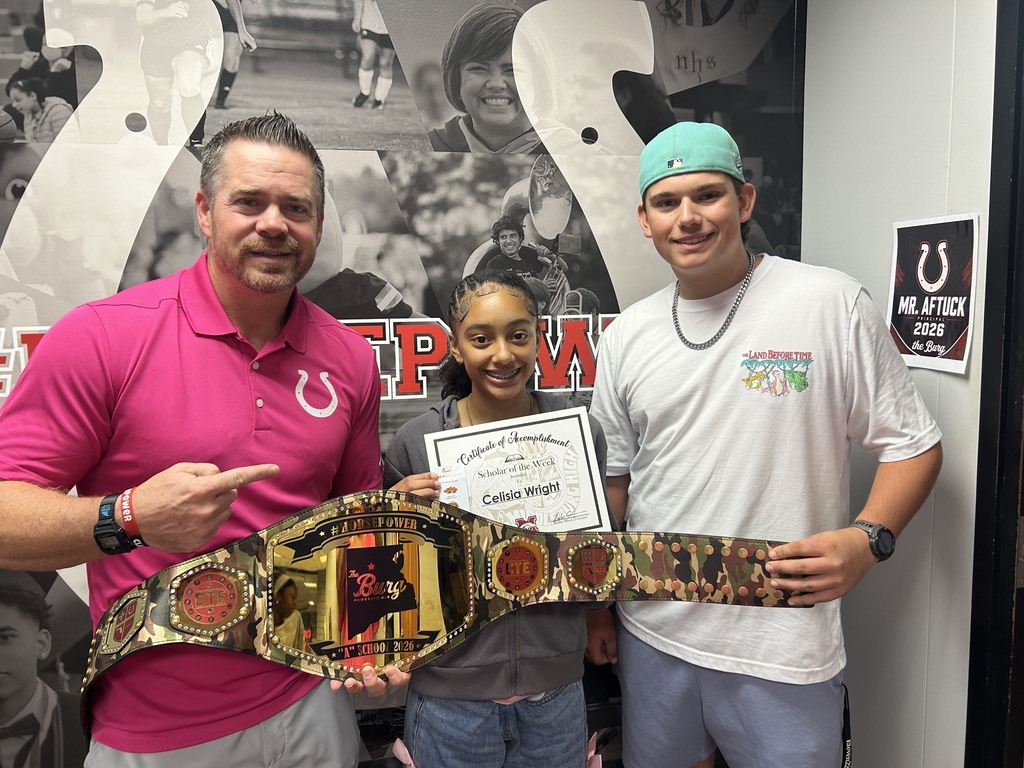 Two men and a woman pose with a championship belt. One man wears a pink shirt and one a white.