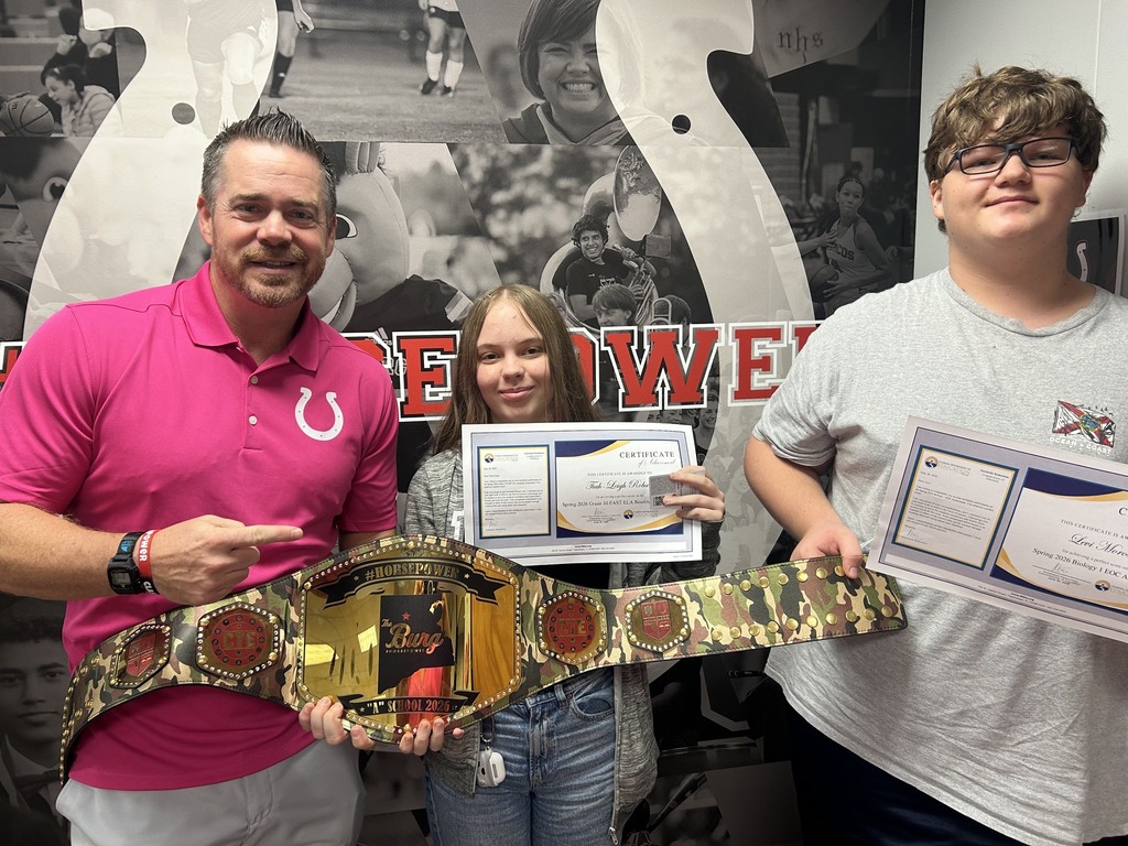 Three people stand together. The two on the sides hold certificates, while the one in the middle holds a belt.