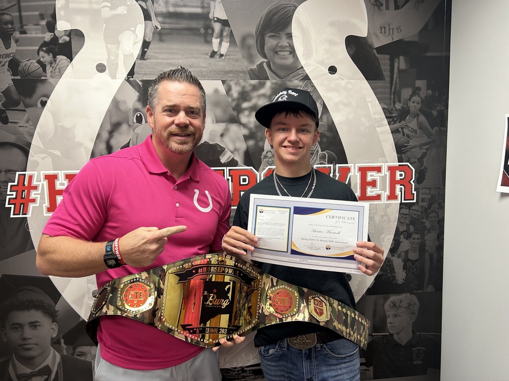 Two men pose with a championship belt and a certificate in front of a sports-themed wall.