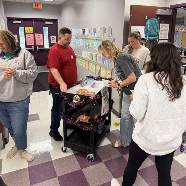 Five people stand in a hallway, two looking at a cart with drinks.