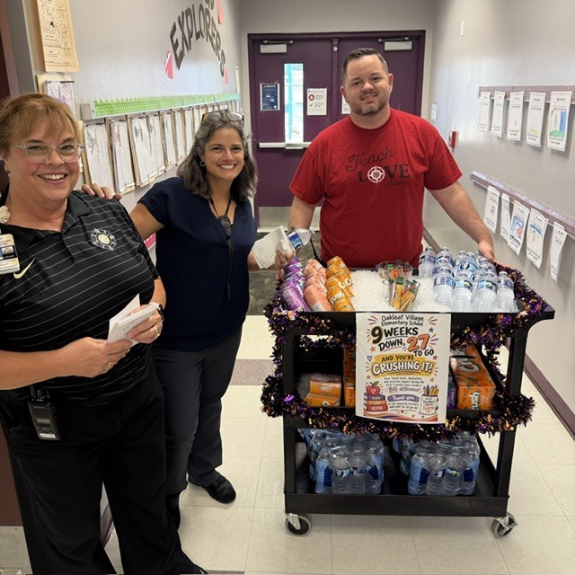 Three people stand near a cart with drinks and tinsel.