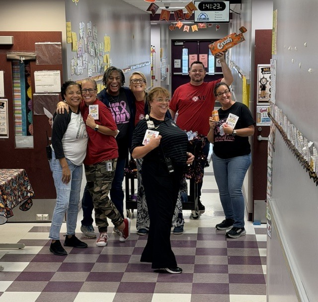 Several people stand in a hallway with a checkered floor. They hold items and pose for a photo.