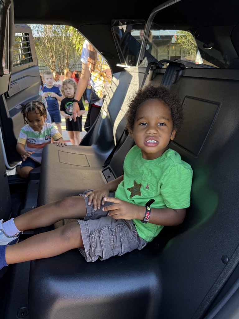 A smiling child sits in a vehicle's back seat. Other children are visible in the background.