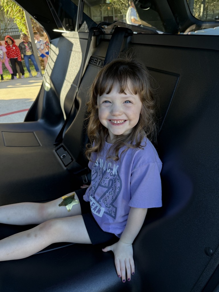 A girl with a bandage on her left leg sits in a vehicle seat and smiles.