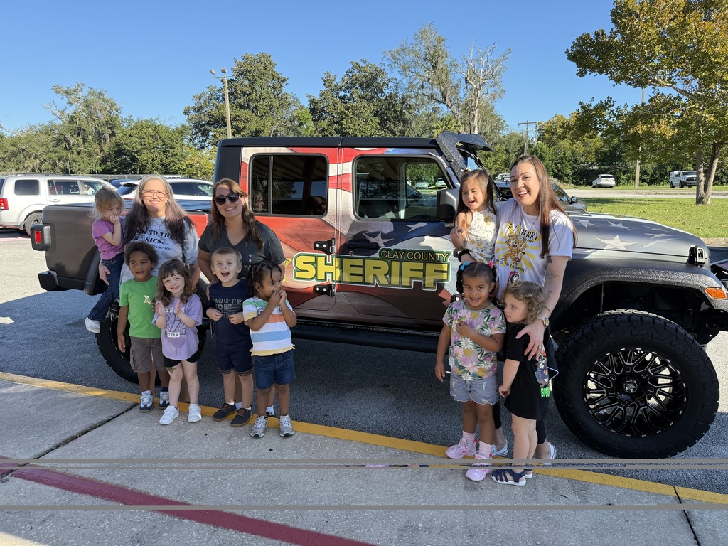 Adults and children pose in front of a large sheriff's vehicle in a parking lot.