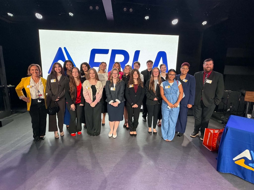 Group of people in suits stand in front of a screen with "FRLA" written in blue.
