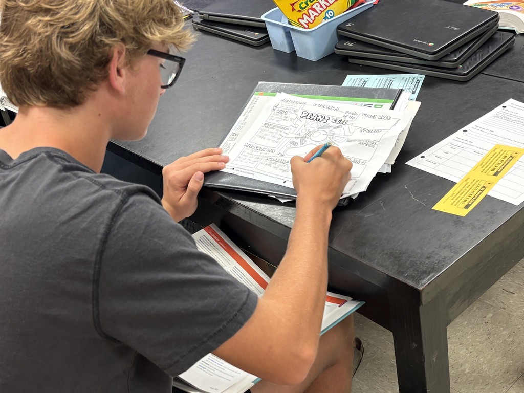 A person wearing glasses seated at a table, using a pen to fill out a form.