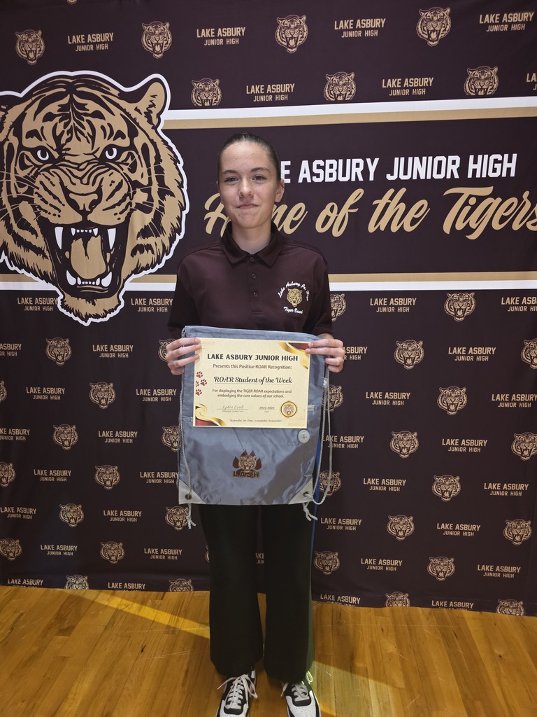 A young person stands with a certificate in front of a wall with a tiger logo.
