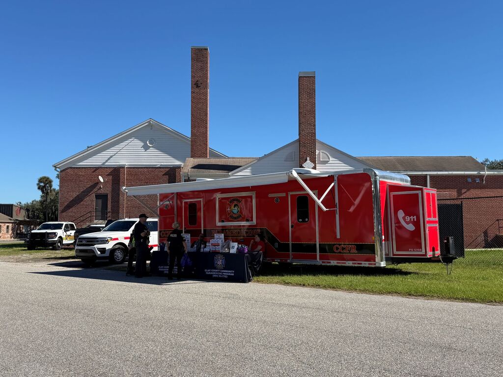Red mobile unit with open canopy parked in front of a large building. People stand around the unit.