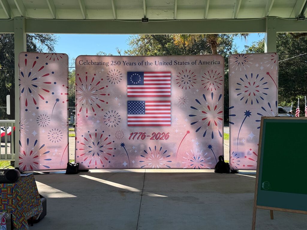 A covered outdoor area displays three pink banners with American flags and fireworks, with a green board on the right.