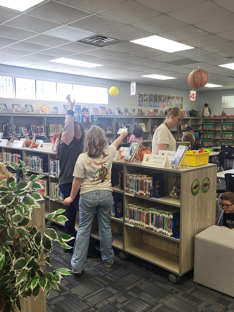 Library staff help a young boy find a book. Staff members stand at a bookshelf. A plant is nearby.