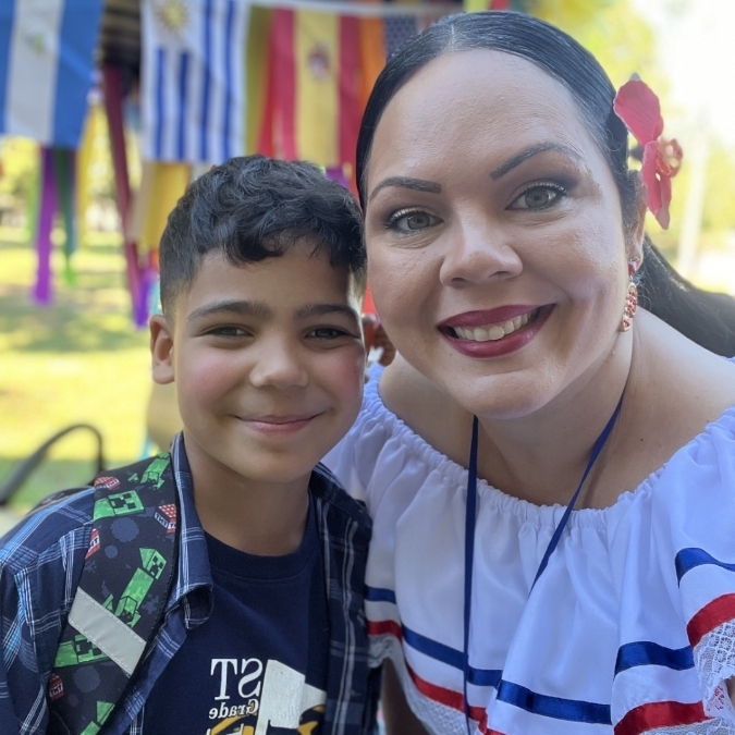 A smiling woman with a red bow in her hair poses with a boy in a colorful shirt.