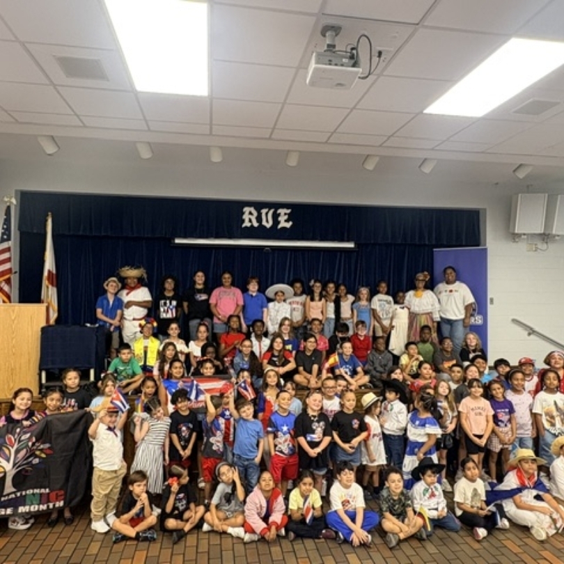 A large group of children and adults pose for a photo in a room with flags.