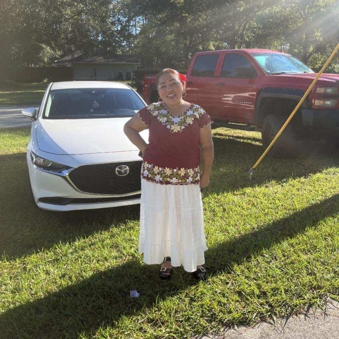 A person stands in a grassy yard next to a white car and a red pickup truck.