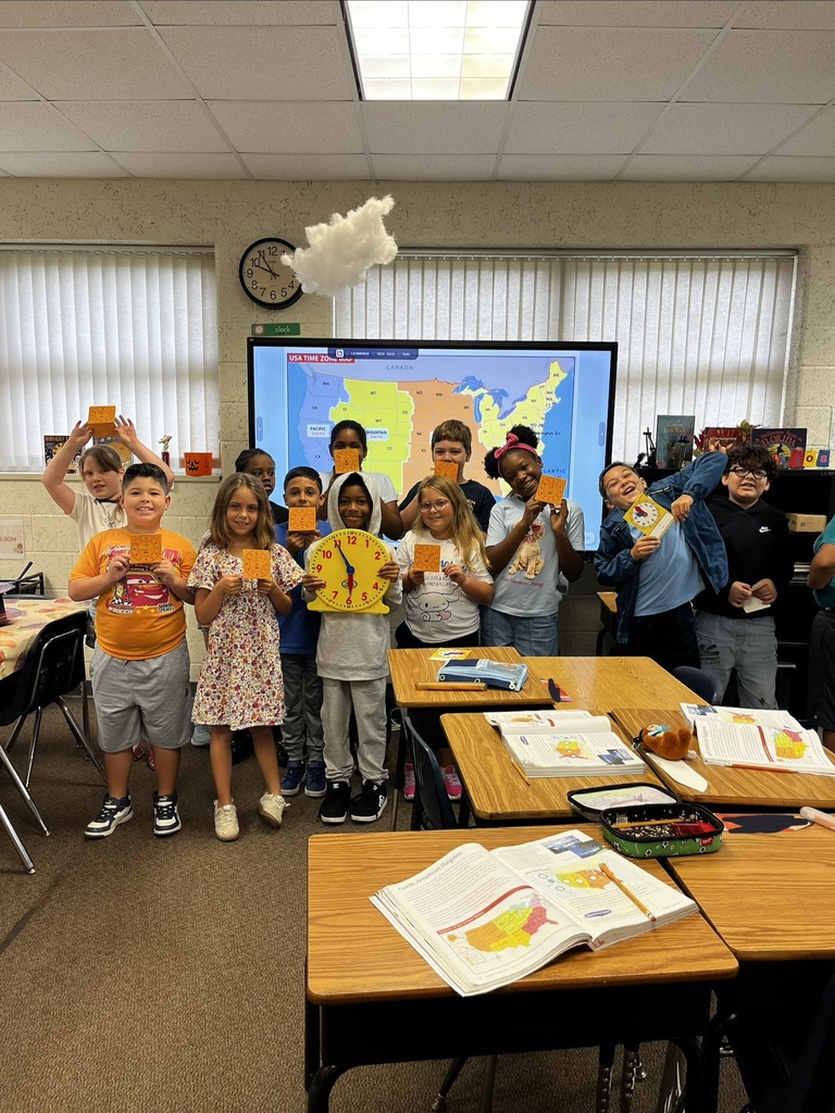 Group of children holding signs in a classroom, with a large map projected on the wall.