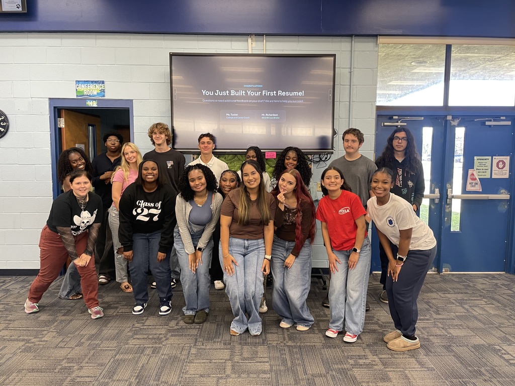 A group of people posing for a photo with a large screen behind them showing a presentation.