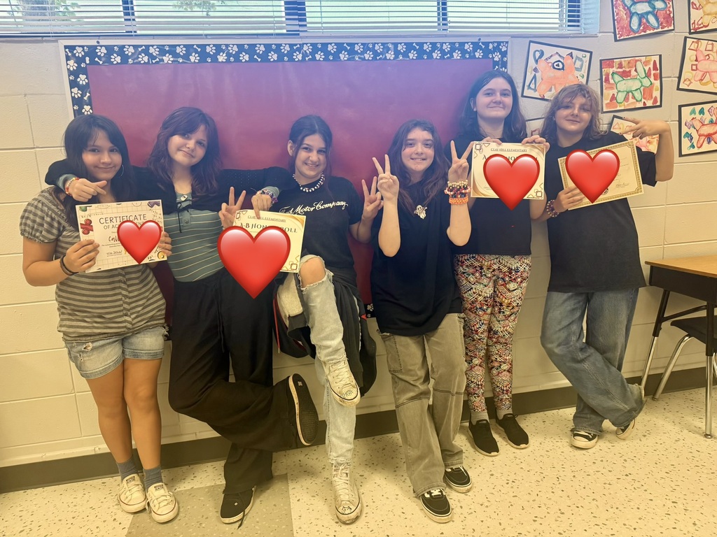 A group of six women pose in a classroom. Each holds a heart-shaped paper in their hands.