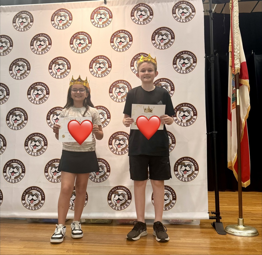 Two children stand in front of a banner with logos, wearing crowns. One holds a red heart, and the other holds a certificate.