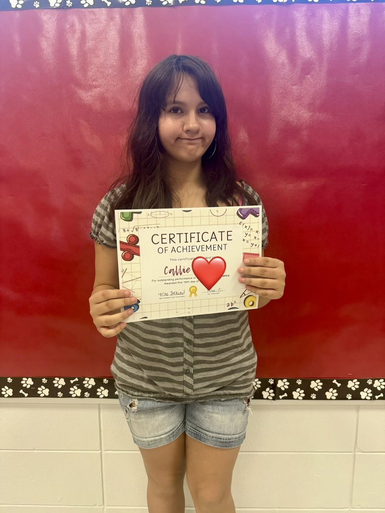 A girl holds a certificate of achievement, smiling, with a red backdrop and a white border.