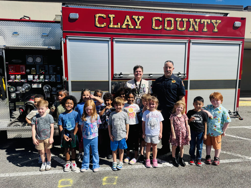 A group of children and adults stand in front of a Clay County fire truck. The adults stand behind the children.