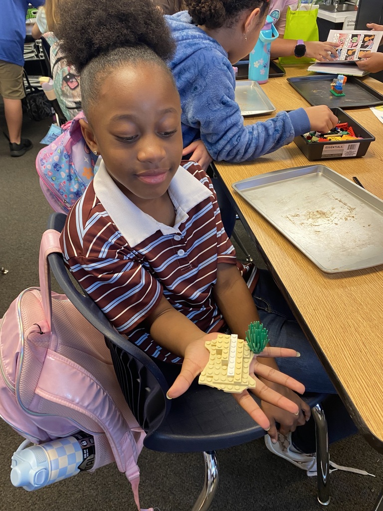 A child with curly hair wearing a striped shirt and white sneakers builds with small objects.
