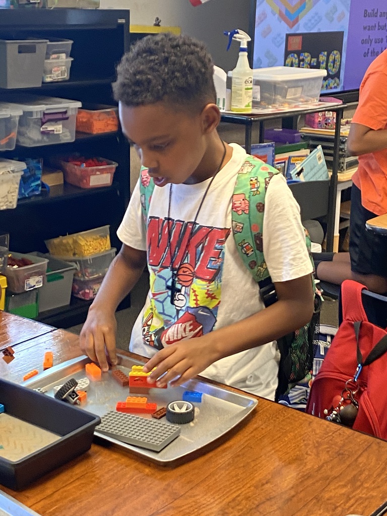 A child wearing a white shirt with a colorful design is constructing a project with colorful building blocks on a table.