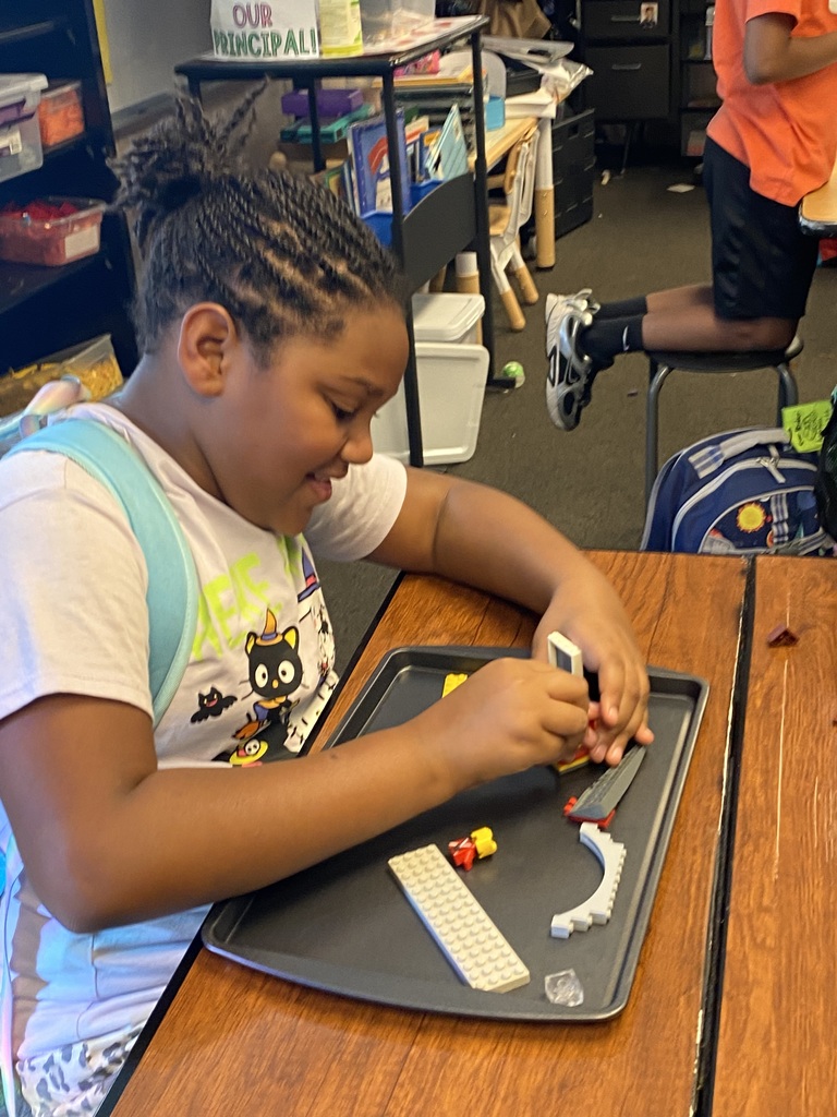 Child in a classroom sitting at a desk, building a structure with Legos on a tray.