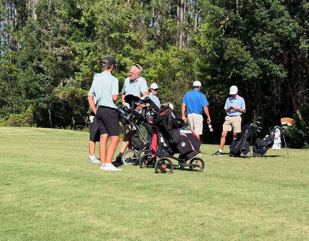 A group of golfers wearing hats and sneakers, discussing near a golf cart and clubs on a green field.