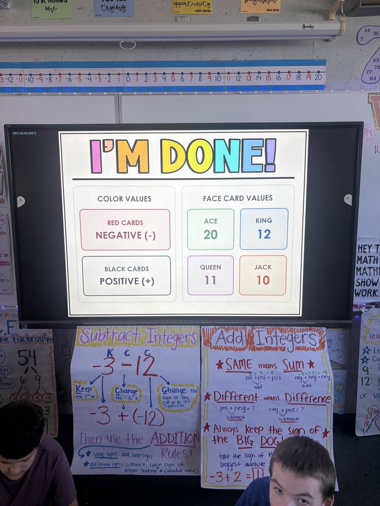 Two boys seated at a desk with a large screen displaying a game with the text "I'm Done!" and numbers.