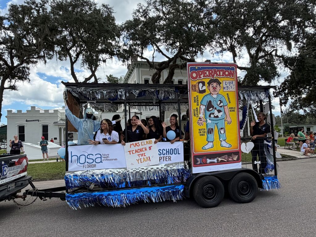 A float trailer with a colorful banner, students on board, parked on the side of a road.
