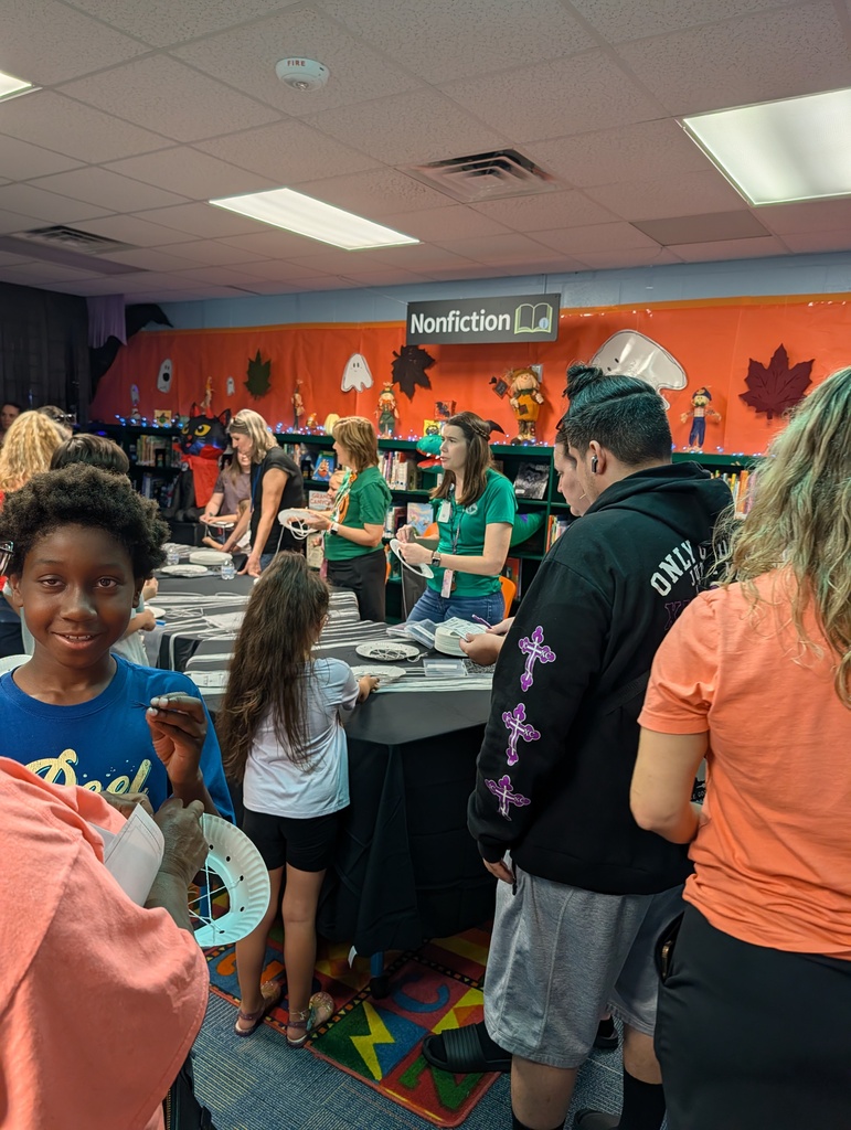 People gather around tables in a brightly colored room, with some individuals standing and others seated.