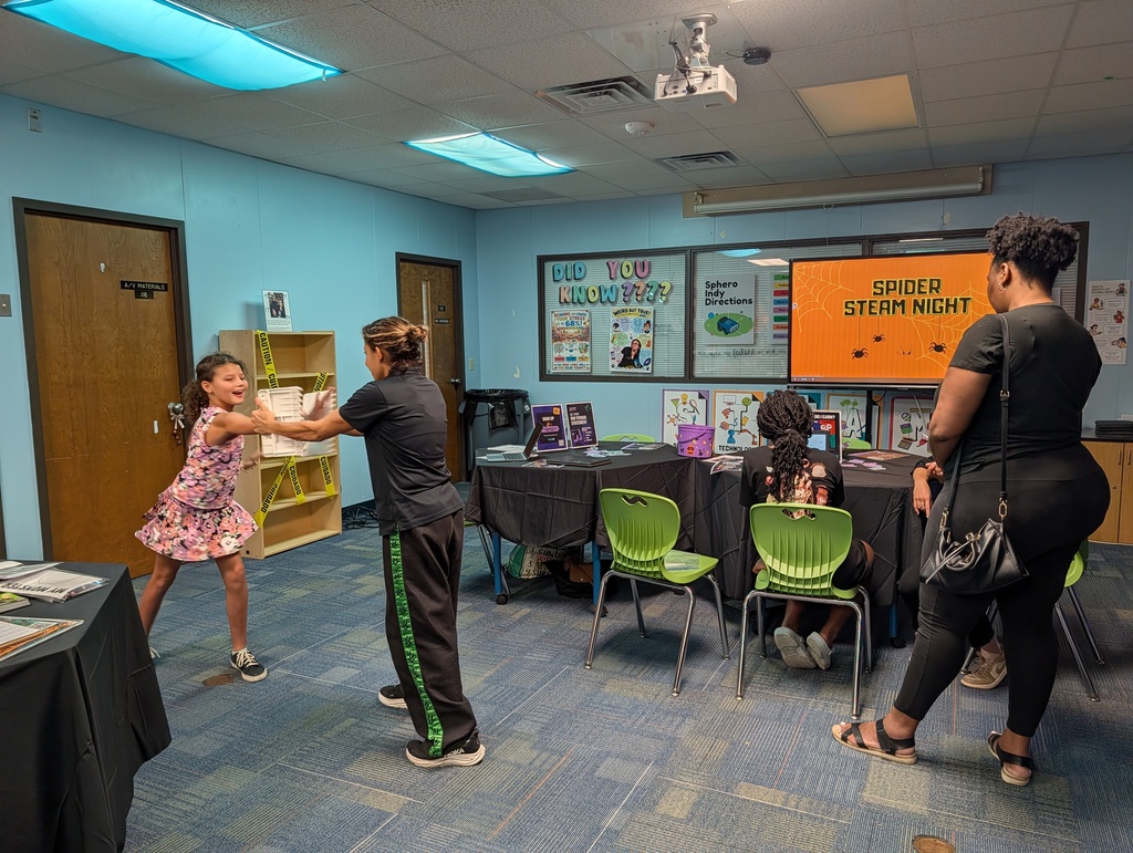 Three adults and two children in a room with tables, chairs, and a sign reading "Spider Stem Night"