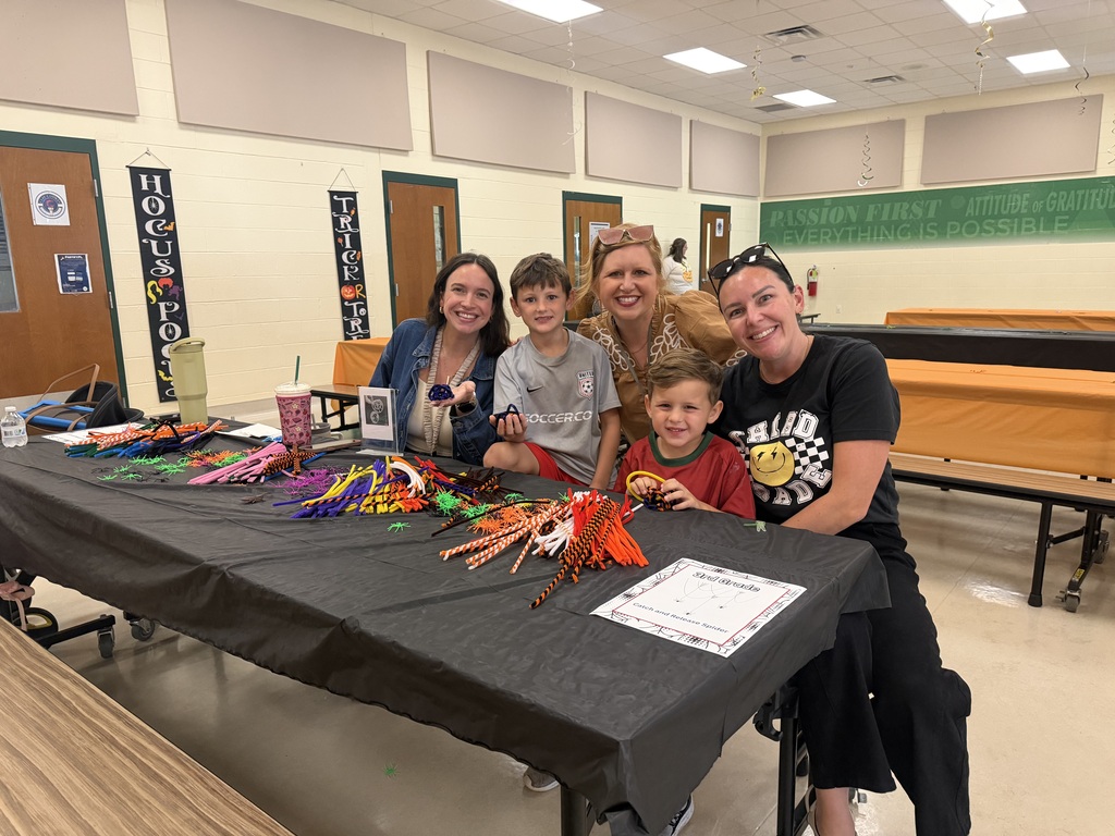 Two women and three children sit at a table with crafts, smiles, and a tablecloth.