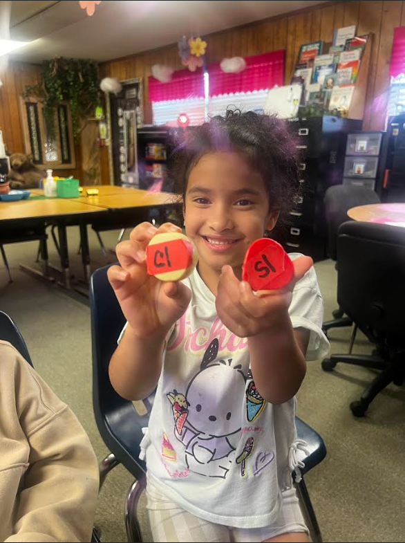 Girl holding two small round objects in classroom. One is red and one is white.