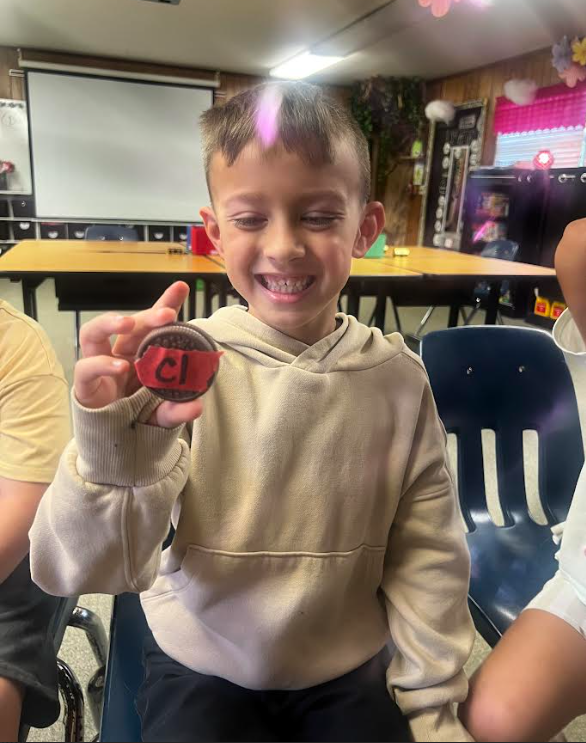 A young boy holds a circular object with a red letter C in a classroom setting.