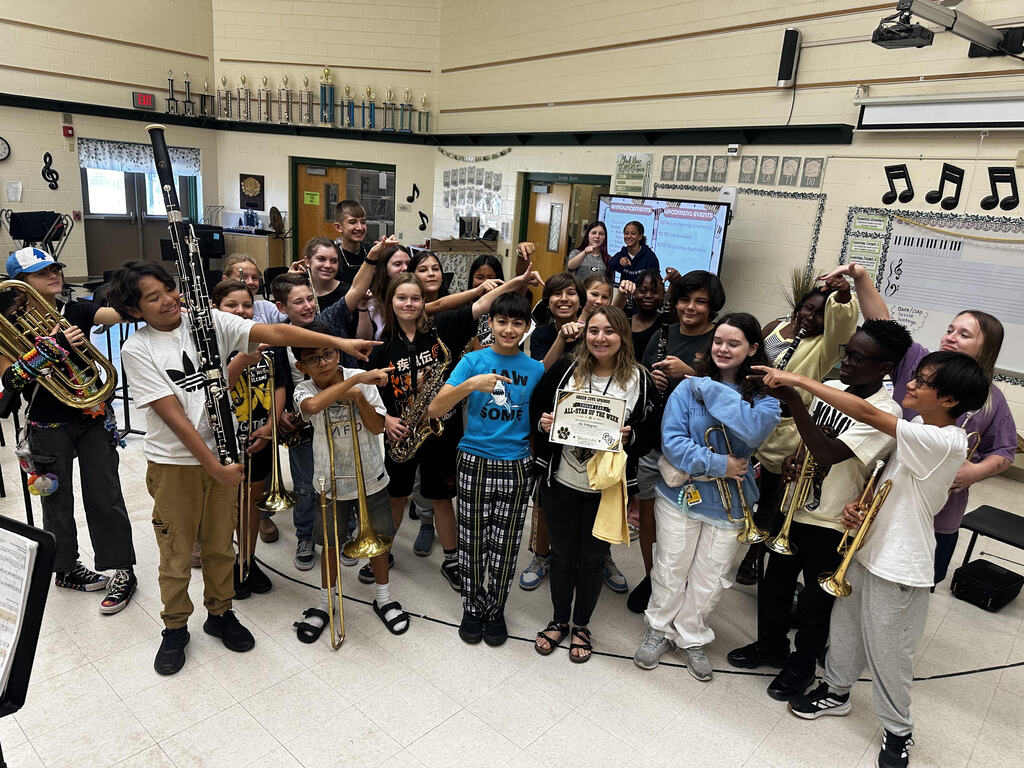 School band members pose with instruments, some holding brass instruments, and some standing around adults.