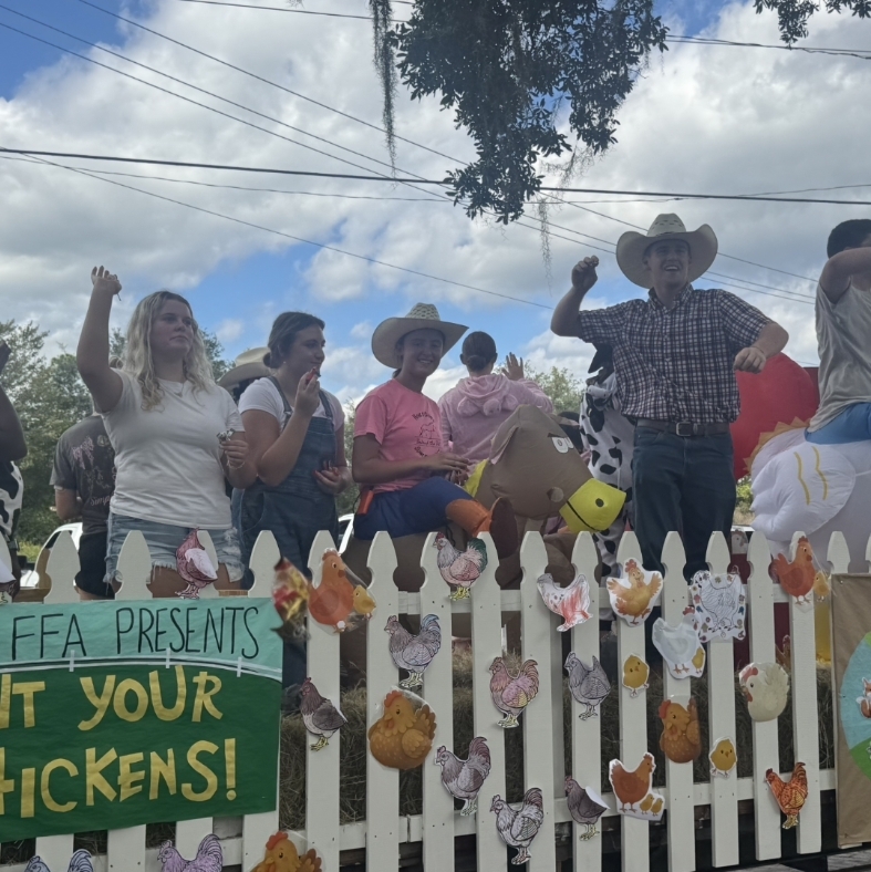 Parade float with white picket fence adorned with paper cutouts of chickens and other farm animals.
