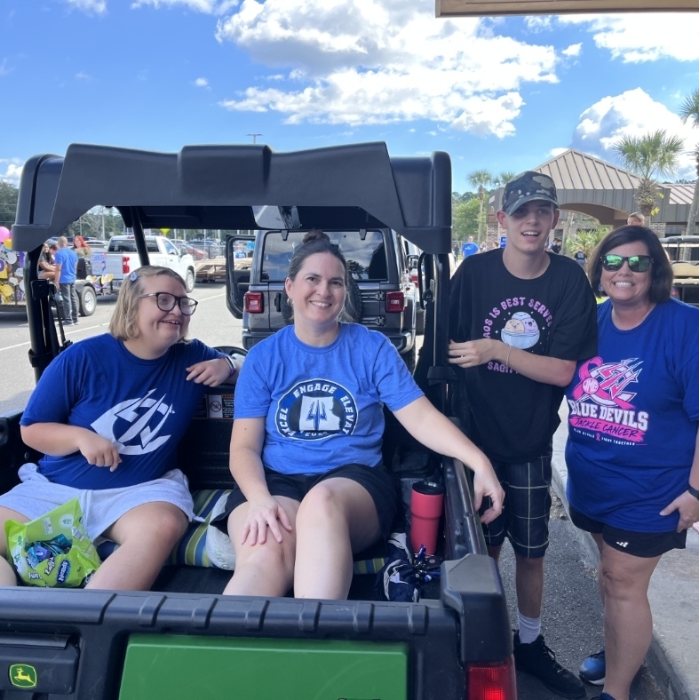 Four adults in blue shirts and hats standing and sitting in the back of a vehicle.